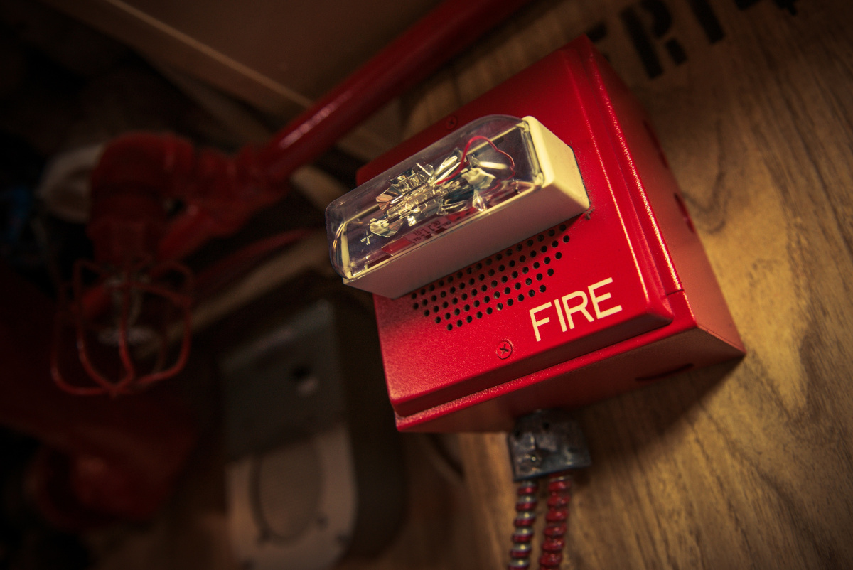 A fire alarm installed on a wall with a fire suppression sprinkler head and pipeline above it in the background