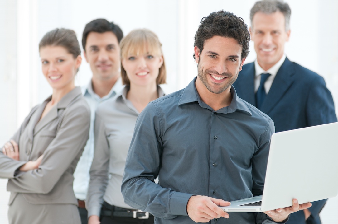 Happy person holding a laptop with his team in the background