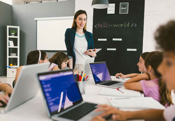 Teacher teaching class full of young children on laptops