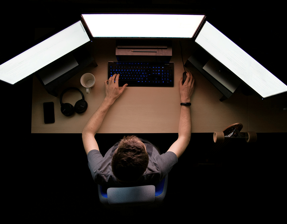 Man sits at a desk with three monitors