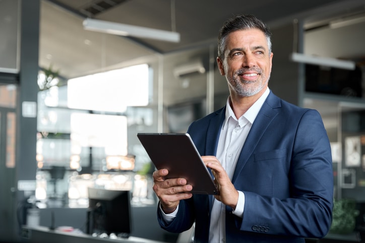 Happy mature business man executive wearing suit in office using tablet.