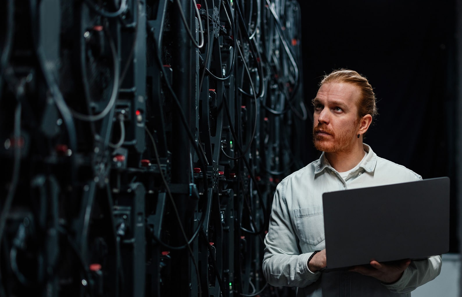 Server technician stands behind server racks holding a laptop