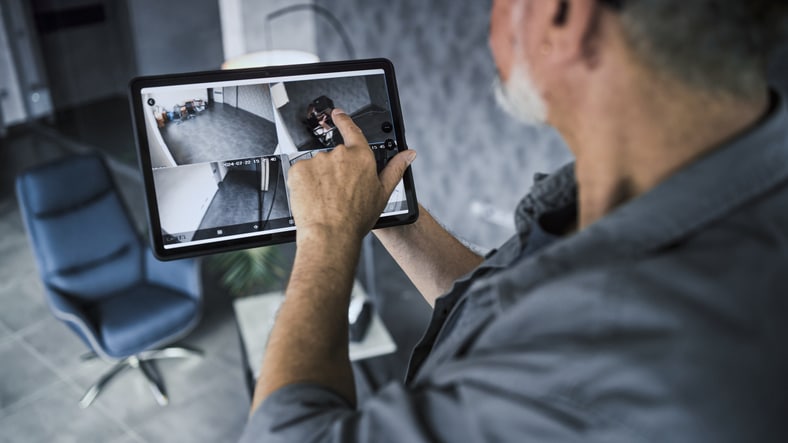 Male installer watches CCTV cameras in stylish office using tablet computer. Real time view of surveillance cameras displayed on tablet screen. Monitoring and tracking. Security system and privacy.