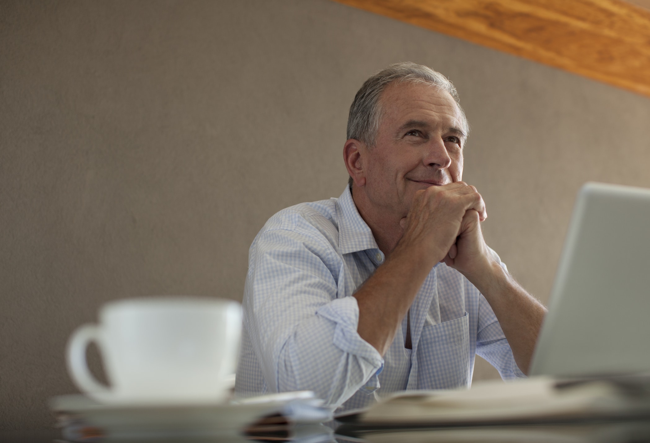 Older man smiling at someone out of frame, sitting at a table with a laptop and coffee cup